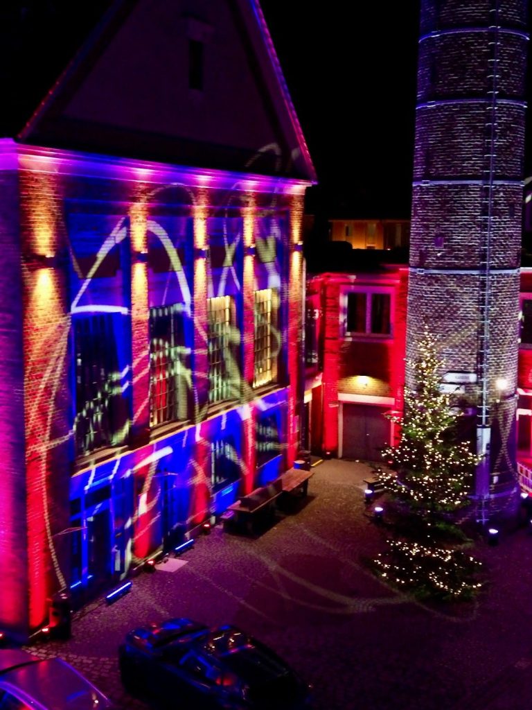 Farbige Lichter erhellen die Fassade eines Gebäudes und einen Weihnachtsbaum.