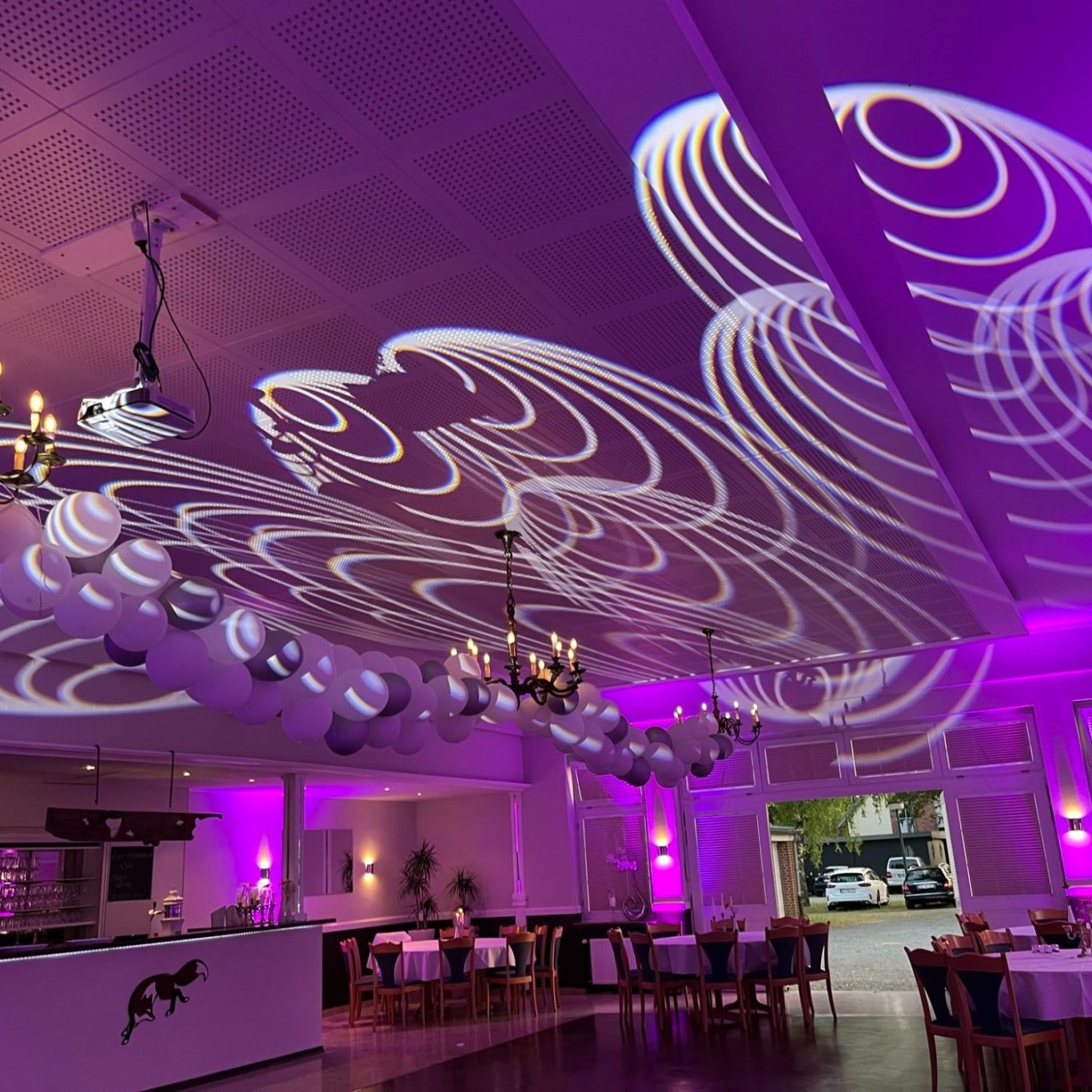 Ein eleganter Veranstaltungssaal mit lila Beleuchtung und kunstvollen Lichtmustern an der Decke.